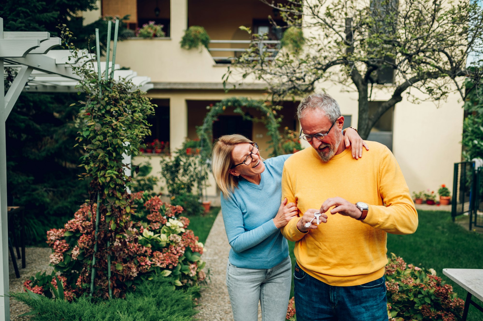 Senior couple holding keys and standing outside their new home
